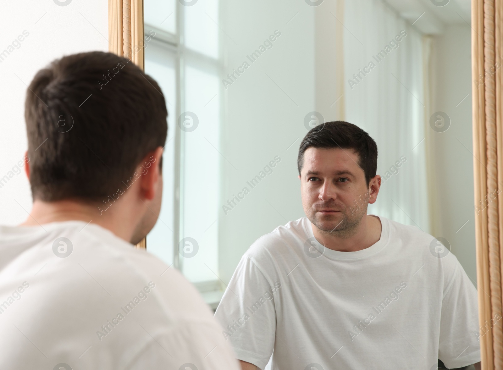 Handsome man looking at himself in mirror indoors Photo of Handsome man looking at himself in mirror indoors
