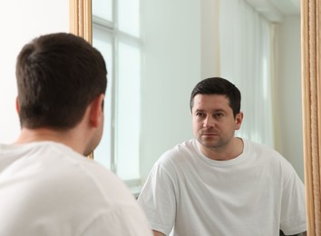 Photo of Handsome man looking at himself in mirror indoors