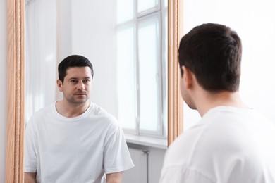 Photo of Handsome man looking at himself in mirror indoors
