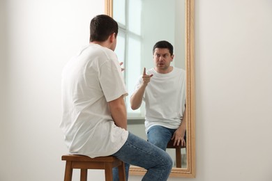 Photo of Handsome man looking at himself in mirror indoors