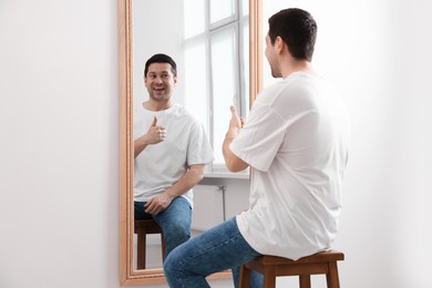 Photo of Handsome man showing thumbs up near mirror indoors