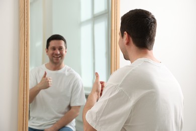 Photo of Handsome man showing thumbs up near mirror indoors