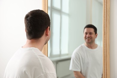Photo of Handsome man looking at himself in mirror indoors