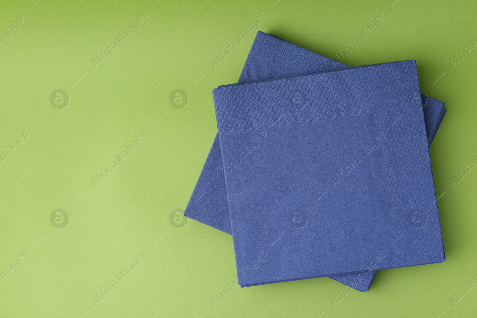 Stack of blue handkerchiefs on green background, top view. Space for text Photo of Stack of blue handkerchiefs on green background, top view. Space for text