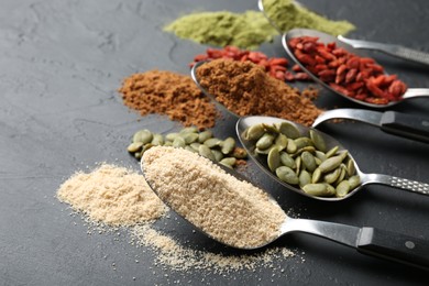Photo of Different superfoods in spoons on black table, closeup. Space for text
