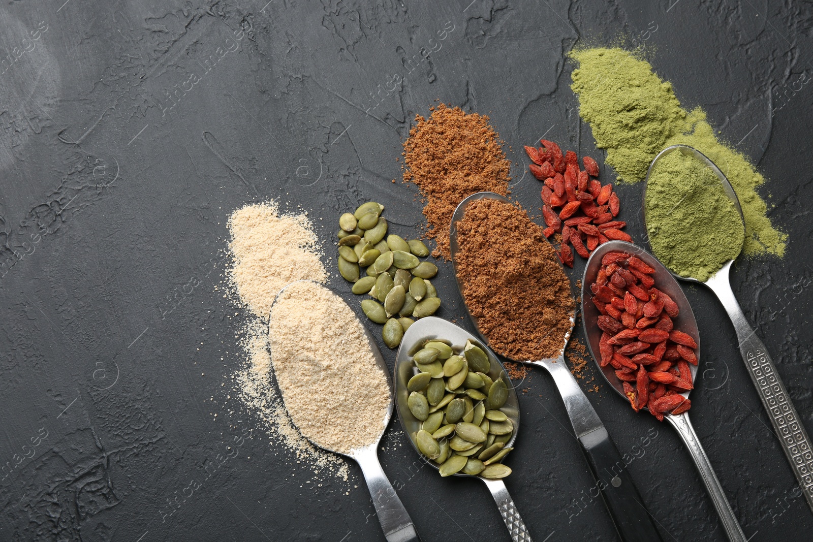 Different superfoods in spoons on black table, flat lay. Space for text Photo of Different superfoods in spoons on black table, flat lay. Space for text