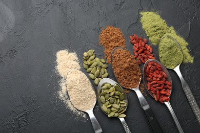 Photo of Different superfoods in spoons on black table, flat lay. Space for text