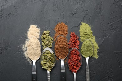 Photo of Different superfoods in spoons on black table, flat lay
