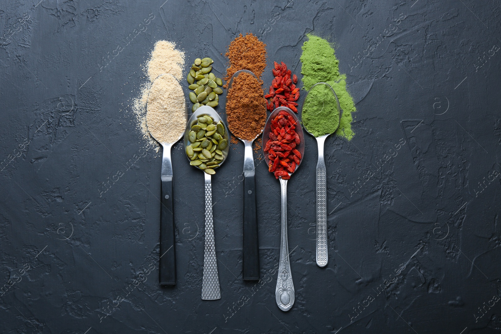 Different superfoods in spoons on black table, flat lay Photo of Different superfoods in spoons on black table, flat lay