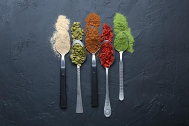 Photo of Different superfoods in spoons on black table, flat lay
