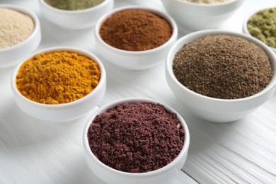 Photo of Different superfood powders in bowls on white wooden table, closeup