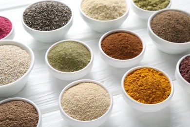 Photo of Different superfood powders in bowls on white wooden table, above view