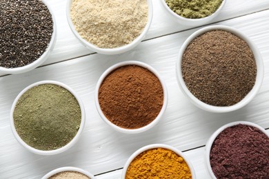 Photo of Different superfood powders in bowls on white wooden table, flat lay
