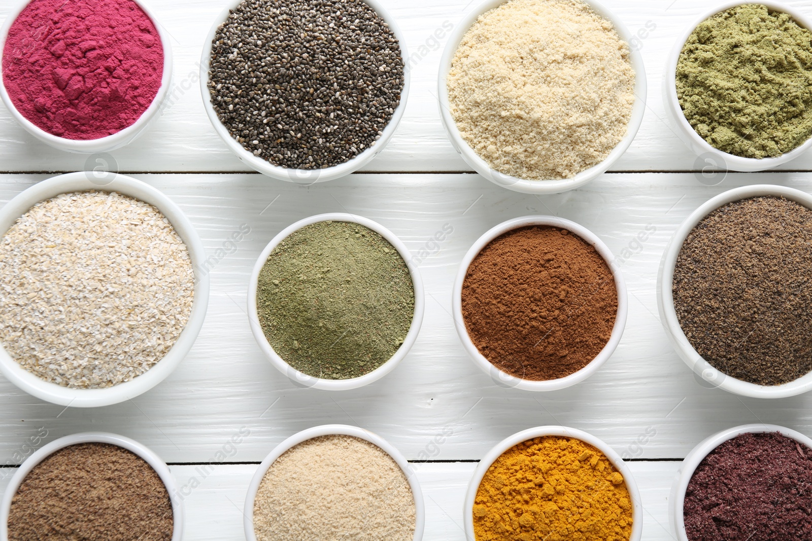 Different superfood powders in bowls on white wooden table, flat lay Photo of Different superfood powders in bowls on white wooden table, flat lay