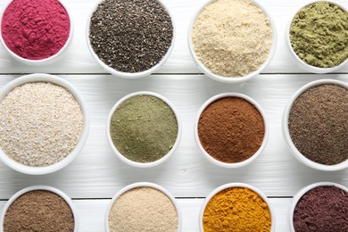 Photo of Different superfood powders in bowls on white wooden table, flat lay