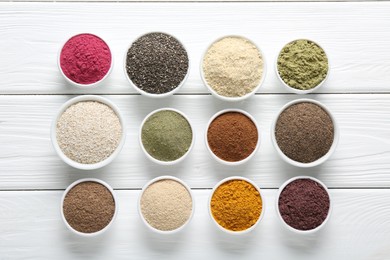 Photo of Different superfood powders in bowls on white wooden table, flat lay