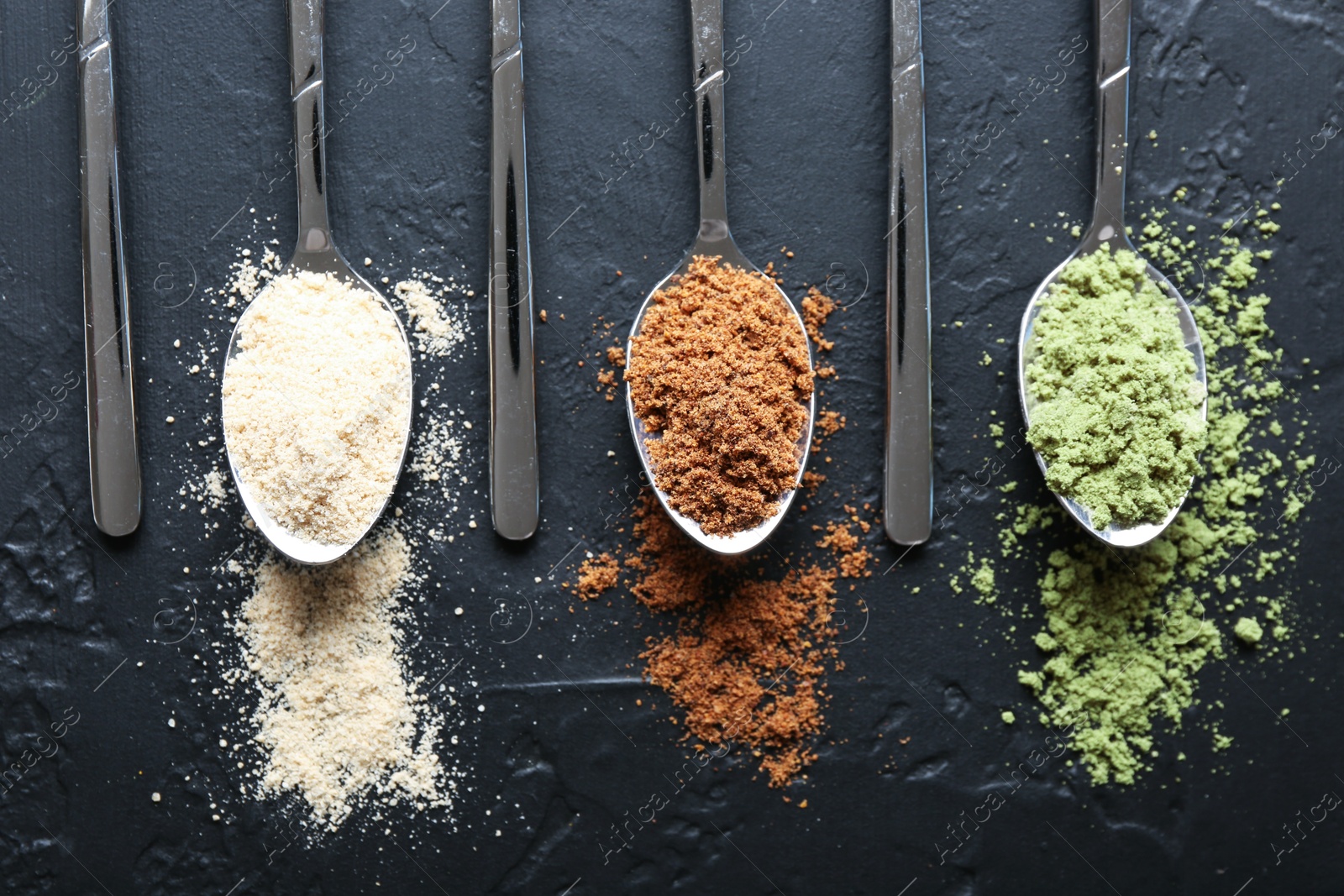 Different superfood powders in spoons on black table, flat lay Photo of Different superfood powders in spoons on black table, flat lay