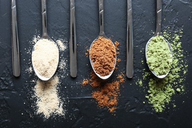 Photo of Different superfood powders in spoons on black table, flat lay