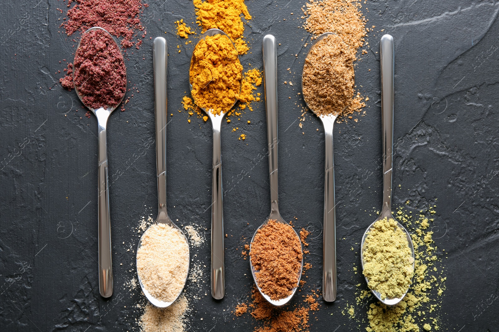 Different superfood powders in spoons on black table, flat lay Photo of Different superfood powders in spoons on black table, flat lay