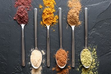 Photo of Different superfood powders in spoons on black table, flat lay