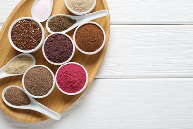 Photo of Different superfoods in bowls and spoons on white wooden table, top view. Space for text