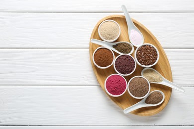Photo of Different superfoods in bowls and spoons on white wooden table, top view. Space for text