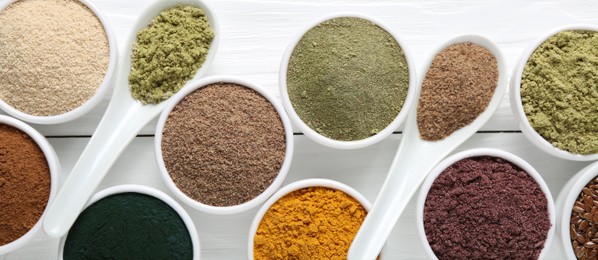 Photo of Different superfood powders in bowls and spoons on white wooden table, flat lay
