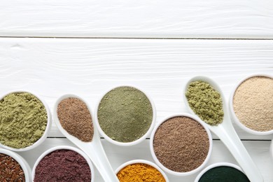 Photo of Different superfood powders in bowls and spoons on white wooden table, flat lay. Space for text