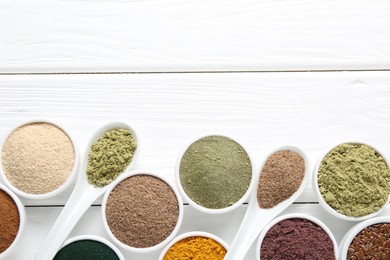 Photo of Different superfood powders in bowls and spoons on white wooden table, flat lay. Space for text