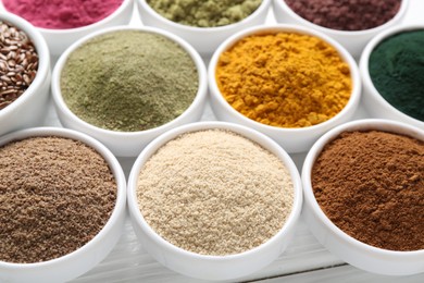 Photo of Different superfood powders in bowls on white wooden table, closeup