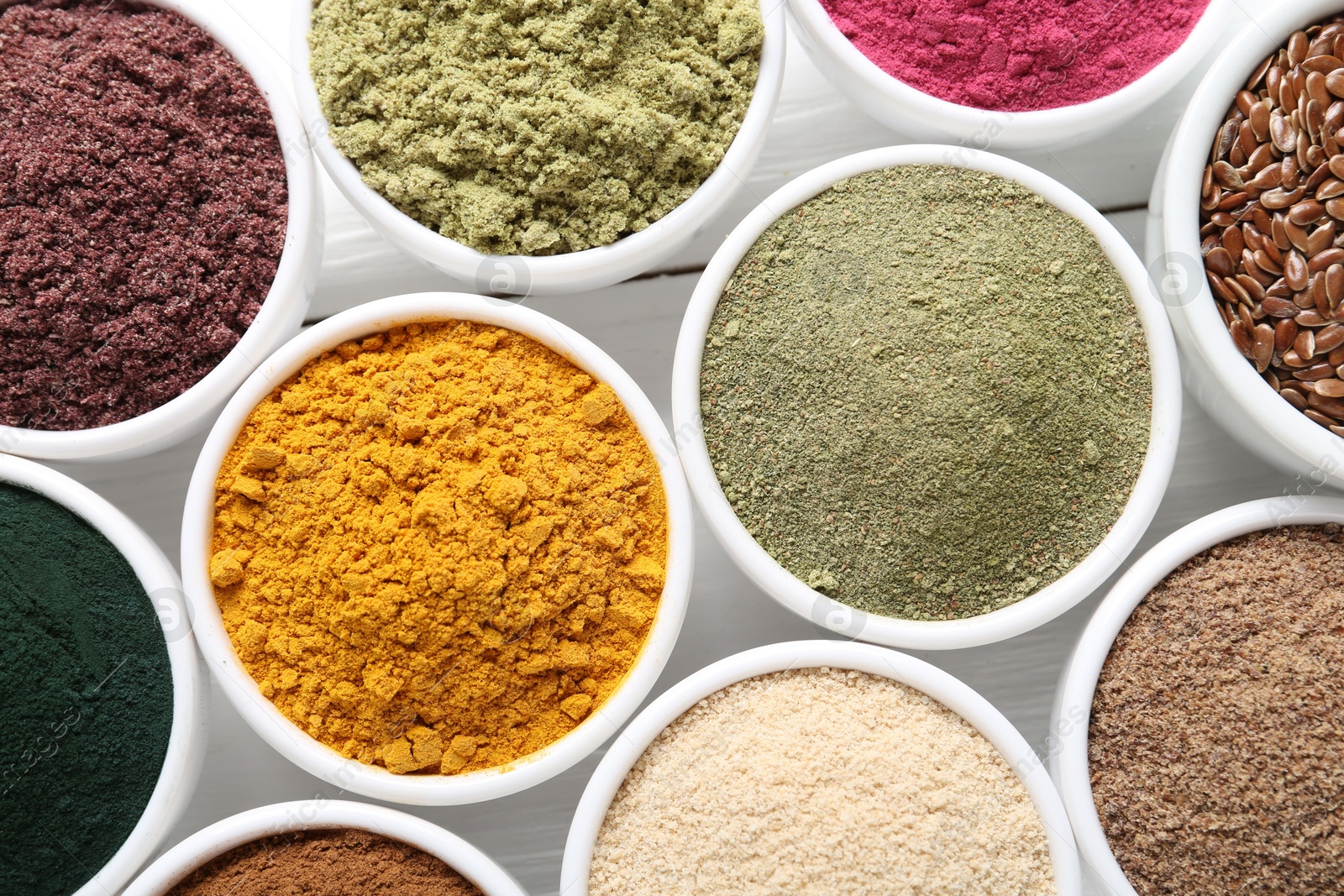 Different superfood powders in bowls on white wooden table, flat lay Photo of Different superfood powders in bowls on white wooden table, flat lay