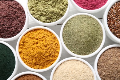 Photo of Different superfood powders in bowls on white wooden table, flat lay