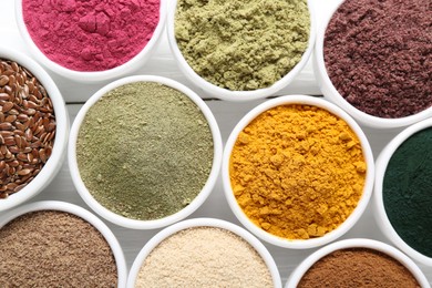Photo of Different superfood powders in bowls on white wooden table, flat lay