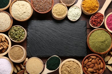 Photo of Different superfood products and blank board on wooden table, flat lay. Space for text