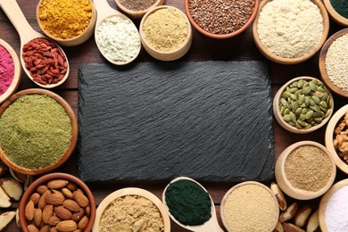 Photo of Different superfood products and blank board on wooden table, flat lay. Space for text