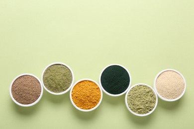 Photo of Different superfood powders in bowls on pale green background, flat lay. Space for text