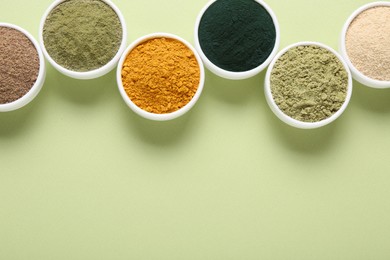 Photo of Different superfood powders in bowls on pale green background, flat lay. Space for text