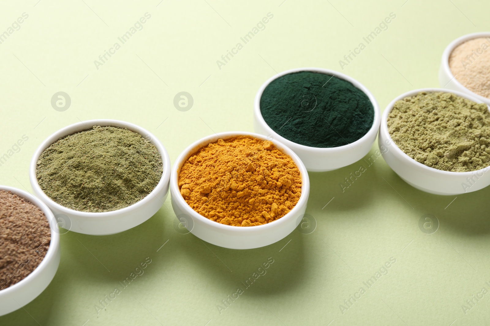 Different superfood powders in bowls on pale green background, closeup Photo of Different superfood powders in bowls on pale green background, closeup