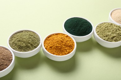 Photo of Different superfood powders in bowls on pale green background, closeup