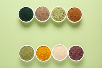 Photo of Different superfood powders in bowls on pale green background, flat lay. Space for text