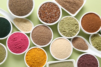 Photo of Different superfood powders in bowls and spoons on pale green background, flat lay