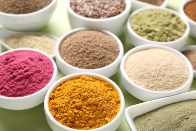 Photo of Different superfood powders in bowls on pale green background, closeup