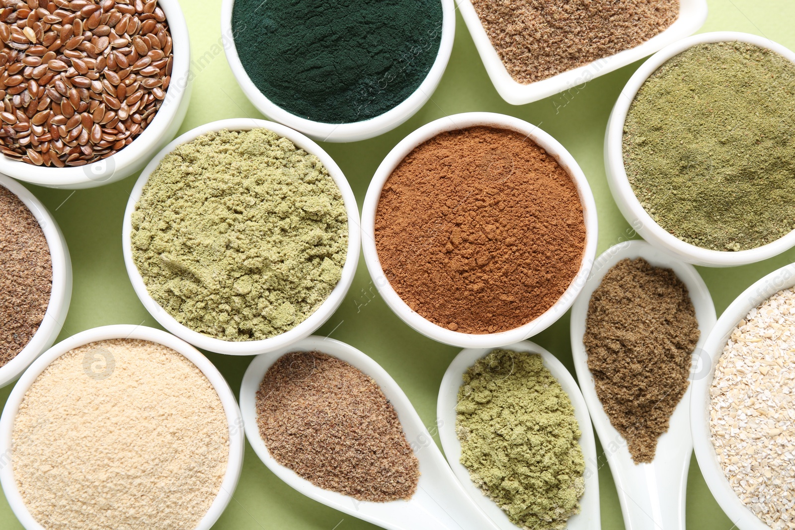 Different superfood powders in bowls and spoons on pale green background, flat lay Photo of Different superfood powders in bowls and spoons on pale green background, flat lay