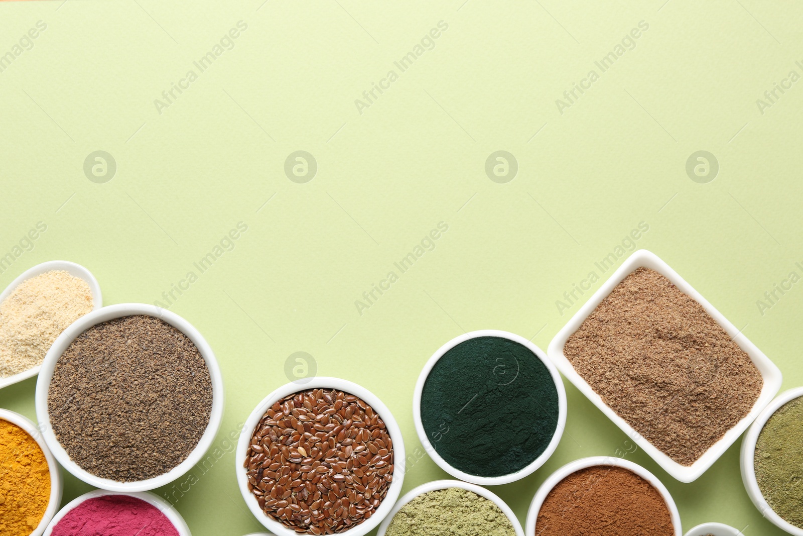 Different superfood powders in bowls on pale green background, flat lay. Space for text Photo of Different superfood powders in bowls on pale green background, flat lay. Space for text
