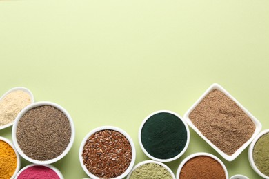 Photo of Different superfood powders in bowls on pale green background, flat lay. Space for text
