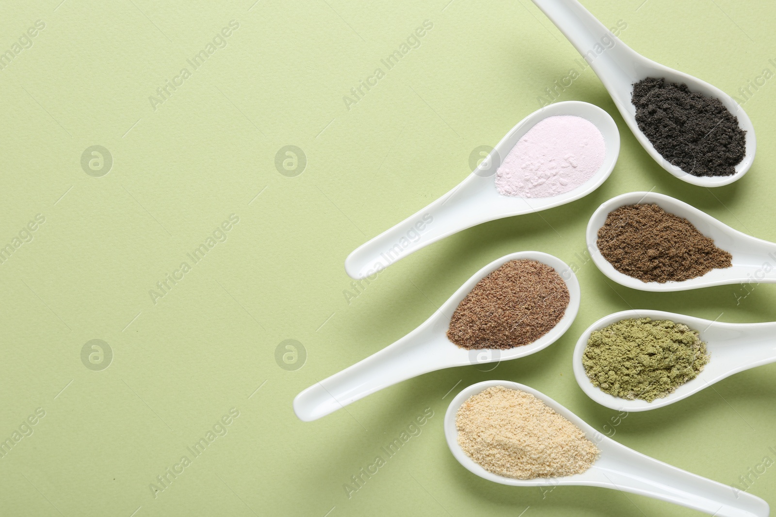 Different superfood powders in spoons on pale green background, flat lay. Space for text Photo of Different superfood powders in spoons on pale green background, flat lay. Space for text
