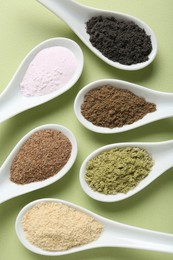 Photo of Different superfood powders in spoons on pale green background, flat lay