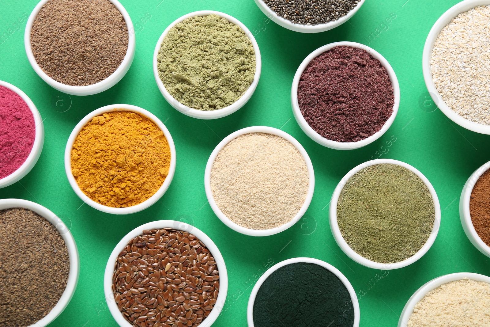 Different superfood powders in bowls on green background, flat lay Photo of Different superfood powders in bowls on green background, flat lay