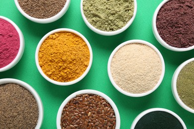 Photo of Different superfood powders in bowls on green background, flat lay