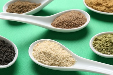 Photo of Different superfood powders in spoons on green background, closeup
